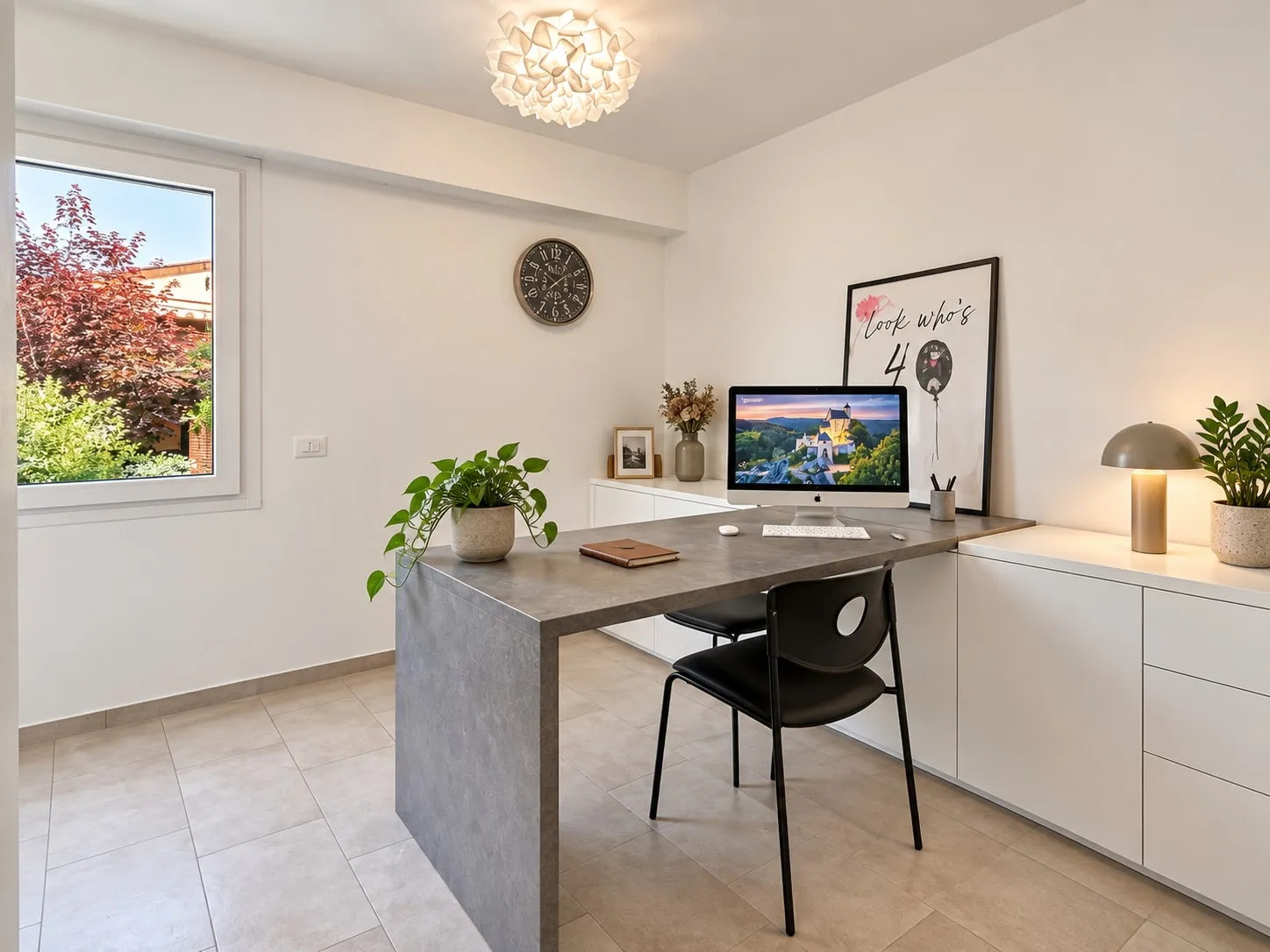 Studio con finestra sul giardino: scrivania in laminato grigio a penisola, mobili bassi bianchi, lampada da tavolo e piante